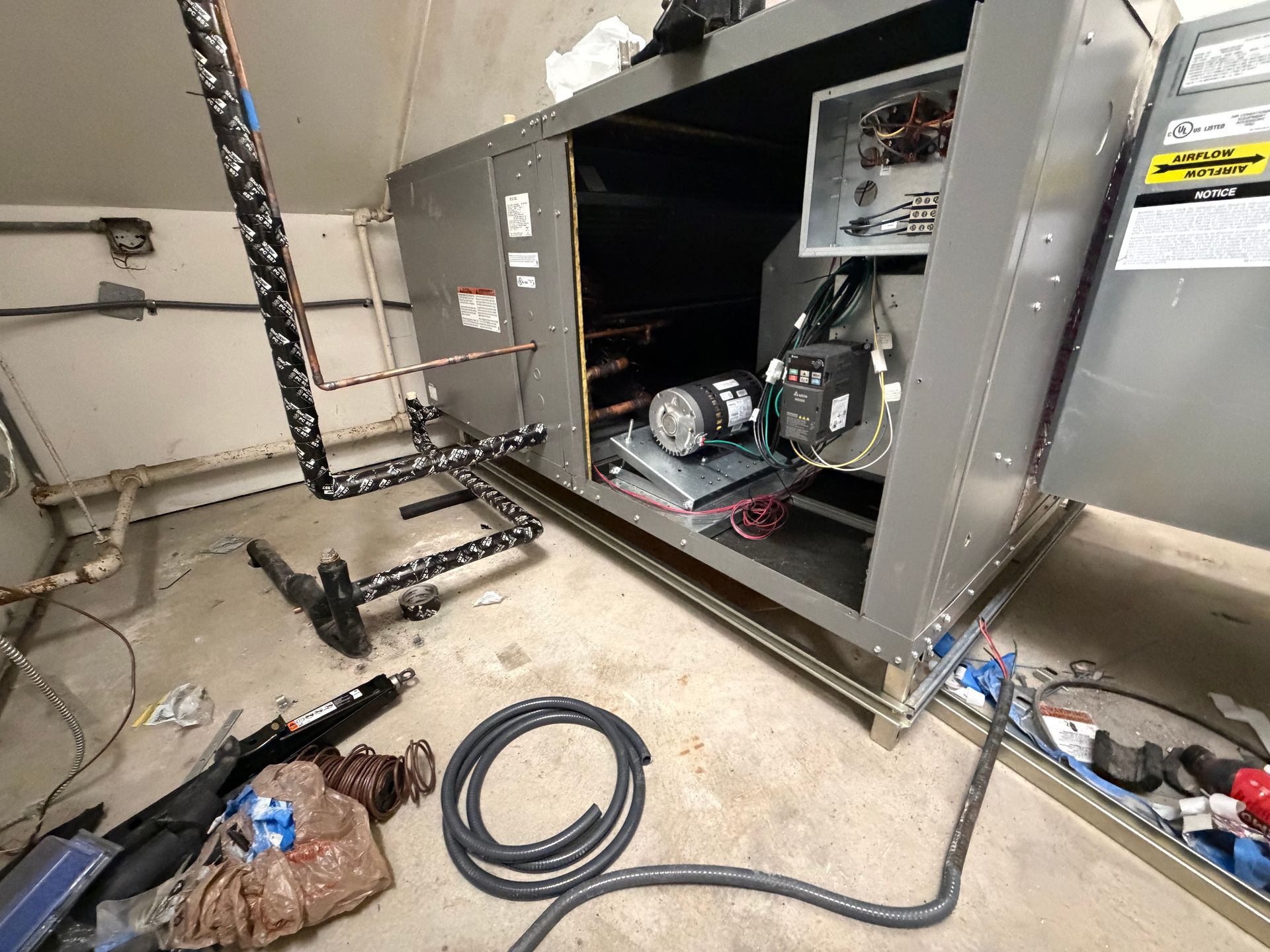 Open HVAC unit with ductwork and tools scattered on the floor in a utility room