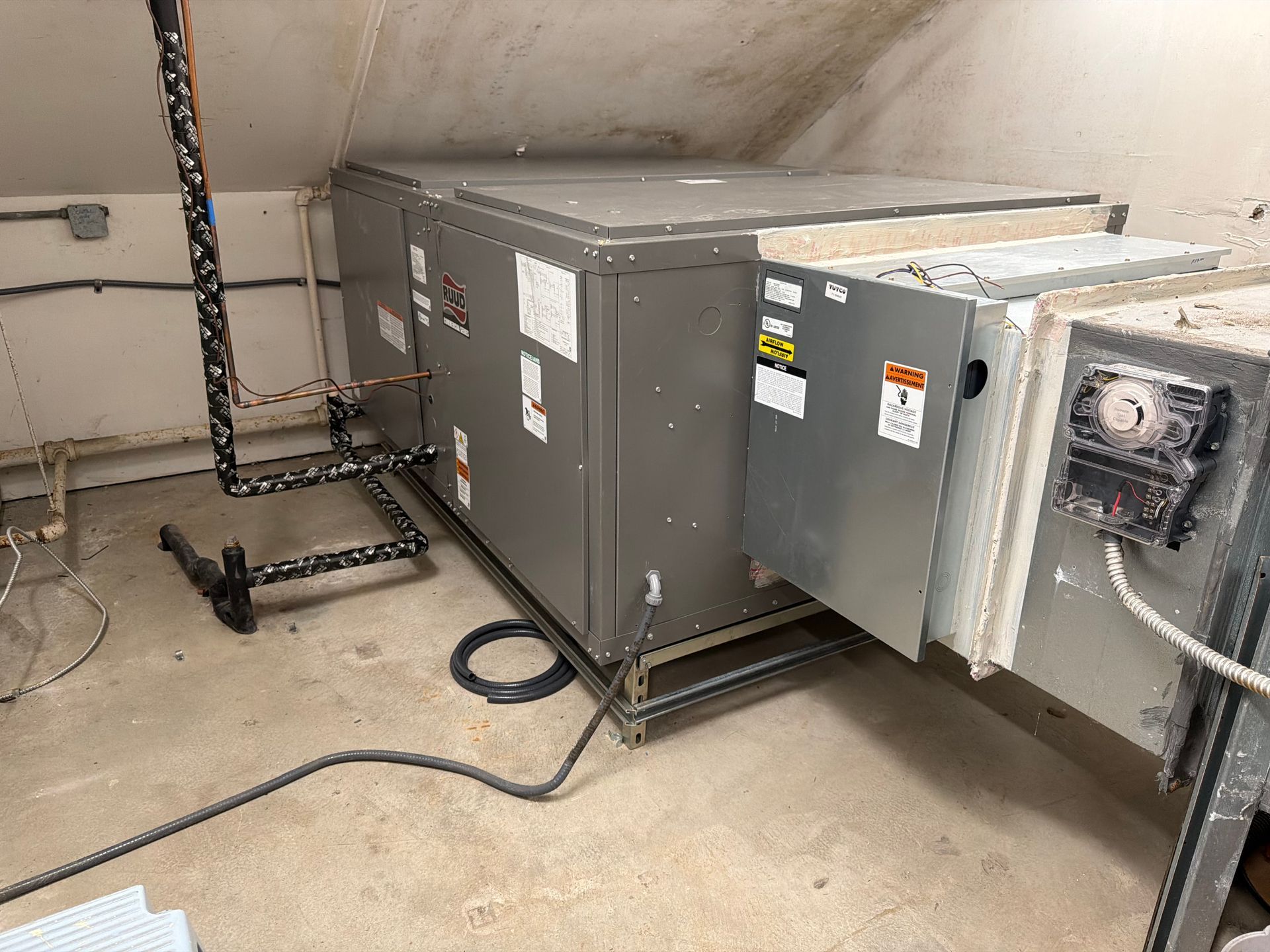 Gray HVAC unit and electrical equipment in a utility room with concrete walls and floor