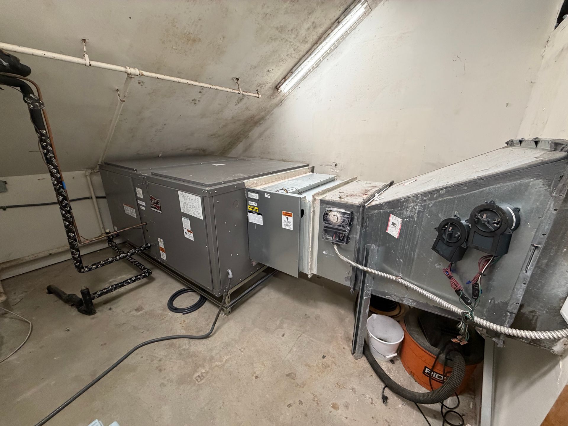 HVAC units and ductwork in a small attic mechanical room with sloped ceiling