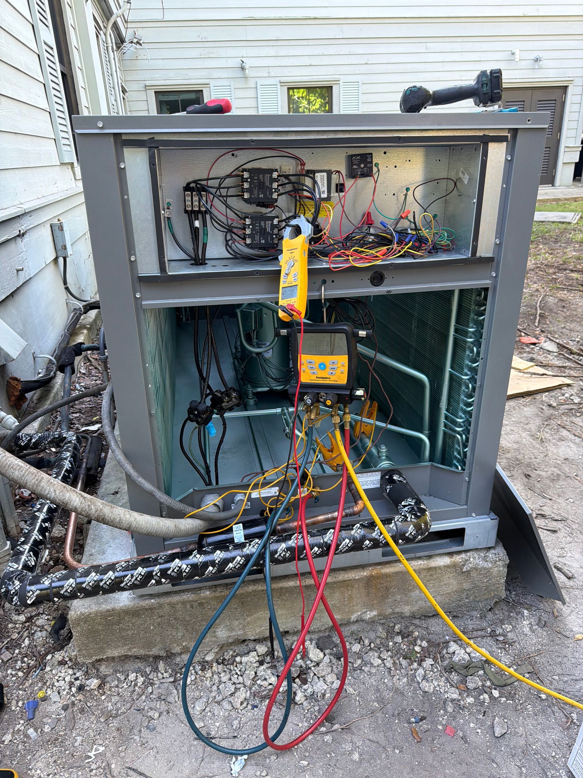 Open electrical HVAC unit with exposed wiring and colored cables outside a house