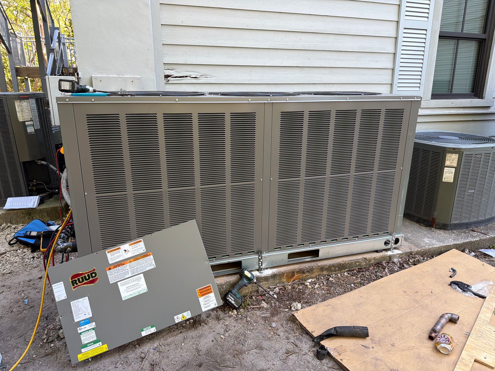 Outdoor HVAC unit beside a house with a detached panel leaning in front of it and tools nearby.