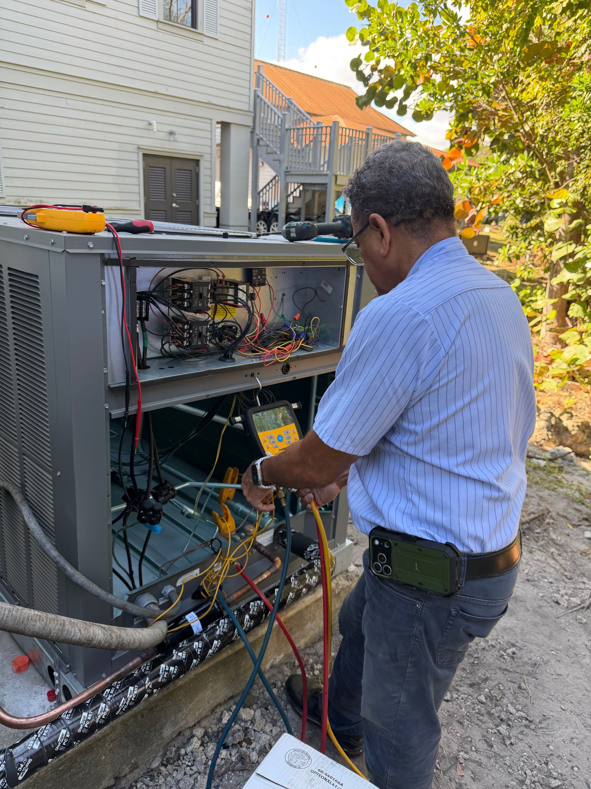 Technician inspecting outdoor electrical equipment beside a building, holding test leads.