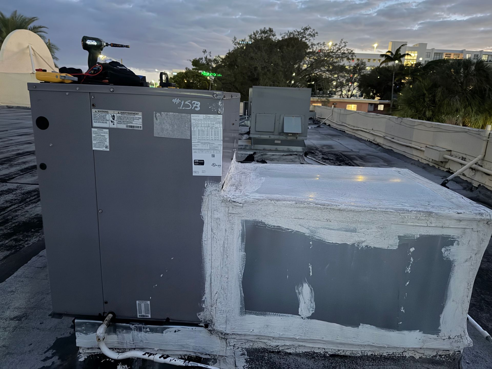 Rooftop HVAC units with gray metal equipment and a white insulated box near a parapet wall.