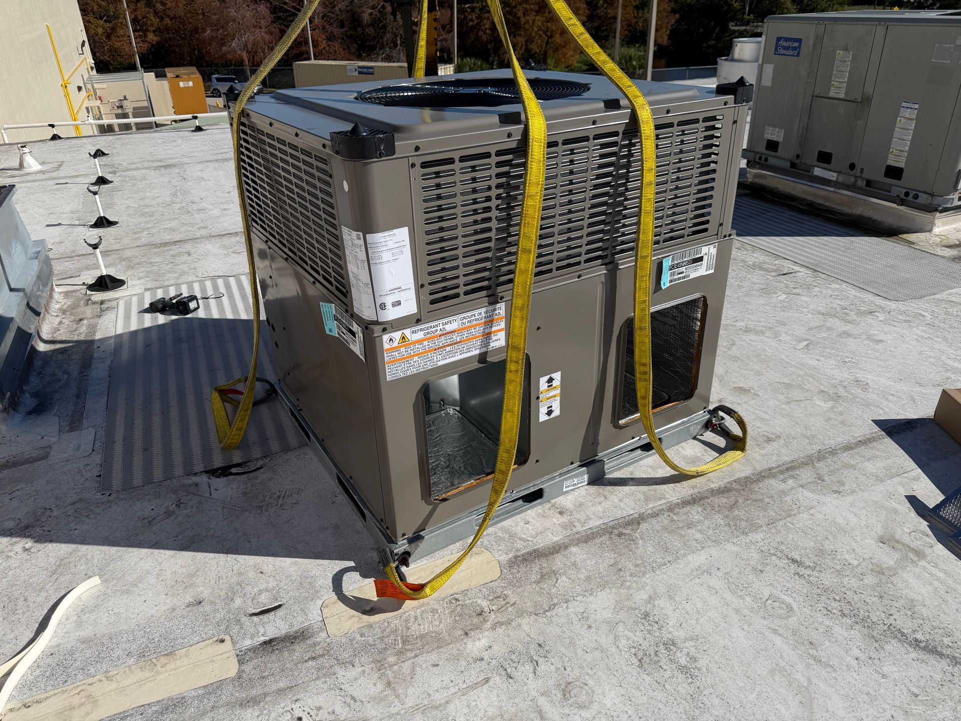 Yellow-strapped rooftop HVAC unit on a flat roof with vents and nearby equipment。