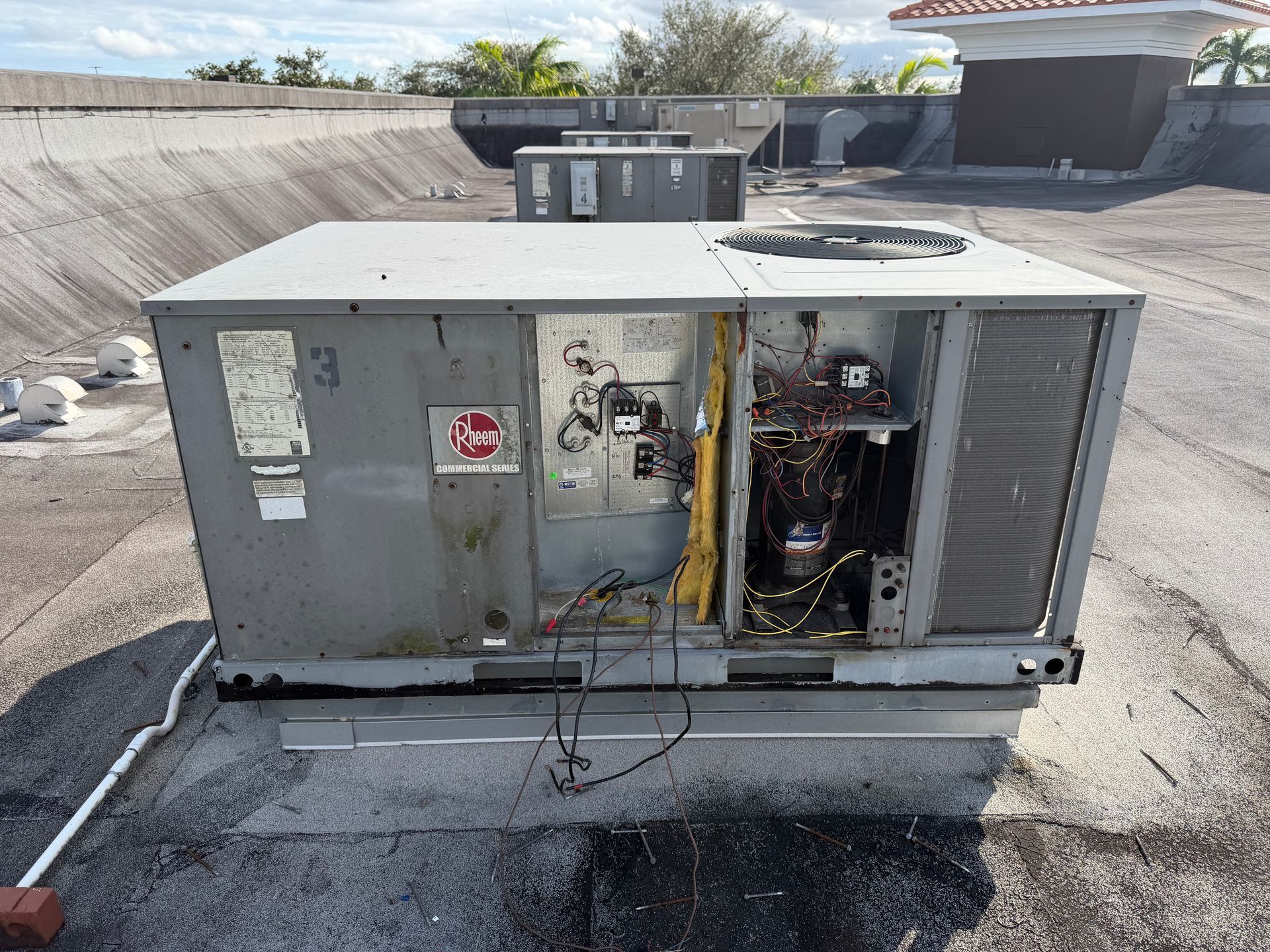 Damaged rooftop HVAC unit with open panel and exposed wiring on a flat roof.