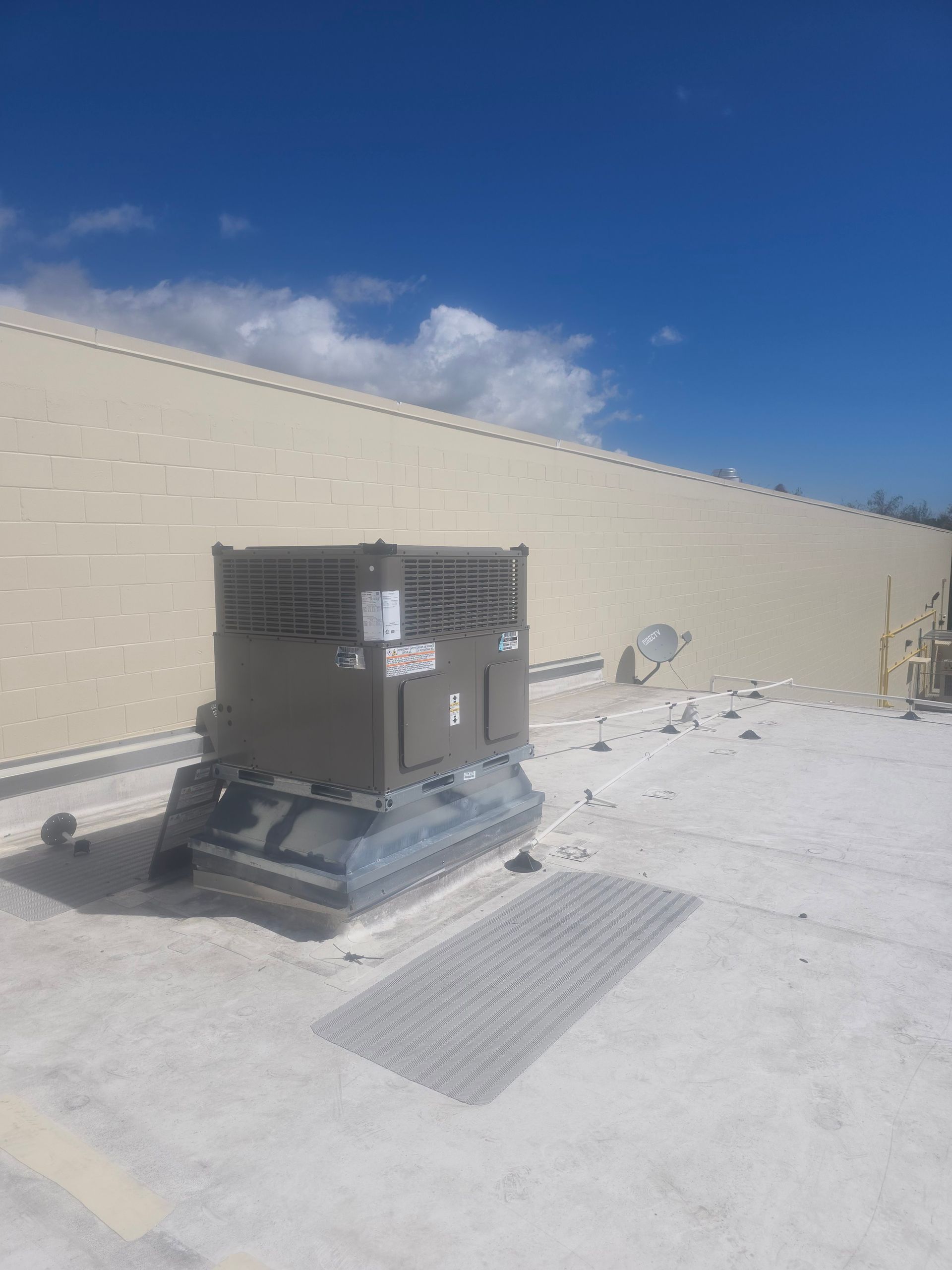 HVAC unit on a rooftop beside a beige wall under a clear blue sky
