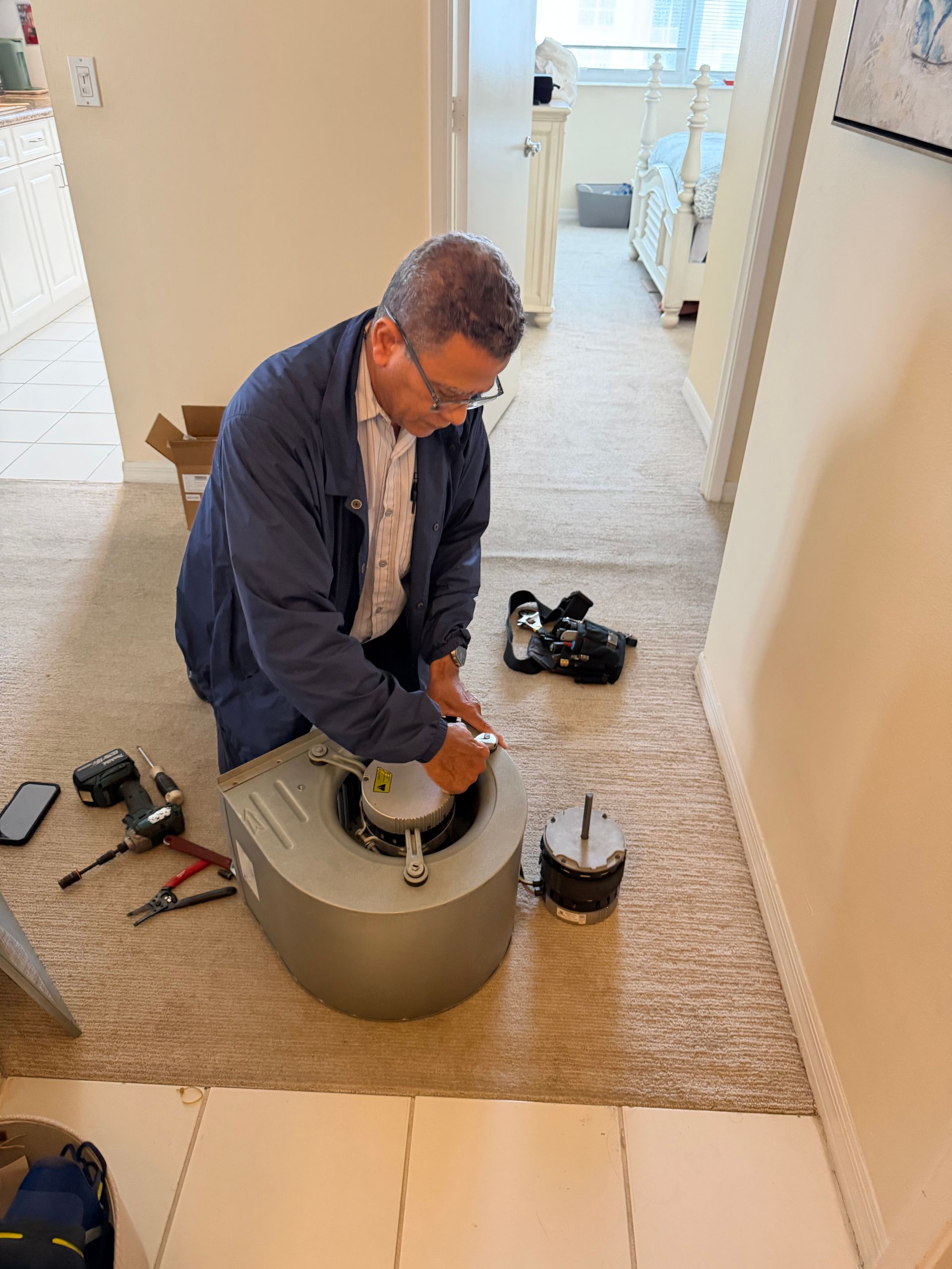 Person kneeling on a carpet, working with a tool on a round metal container in a hallway, shoes nearby