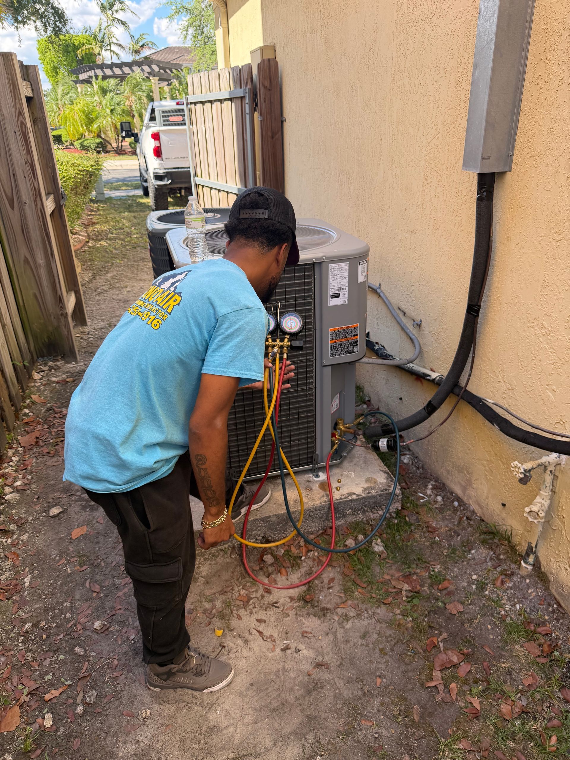 Technician inspecting electrical equipment outdoors beside a building, with cables and tools attached to a unit.