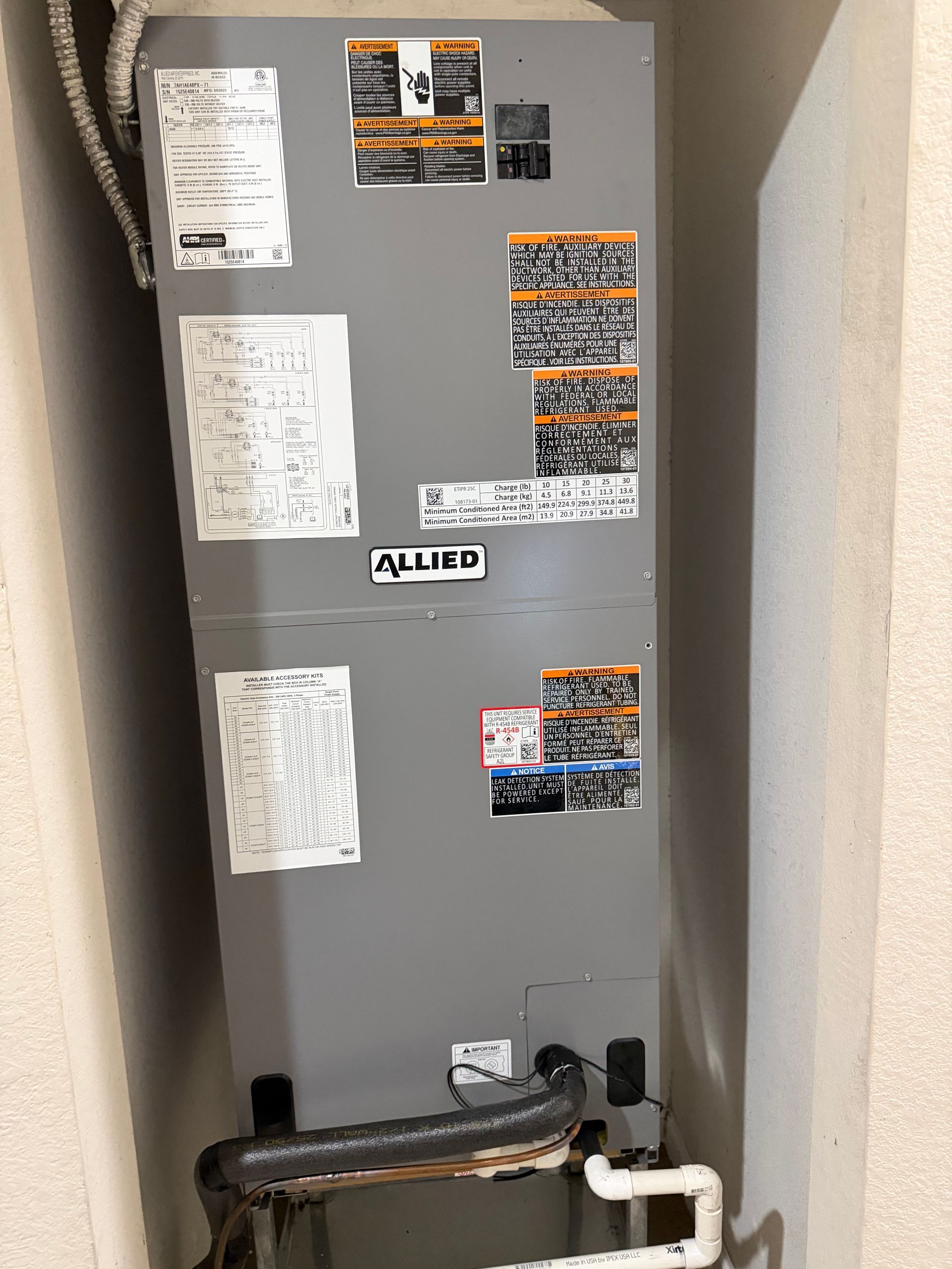 Gray utility furnace in a narrow closet with pipes and warning labels on the front.