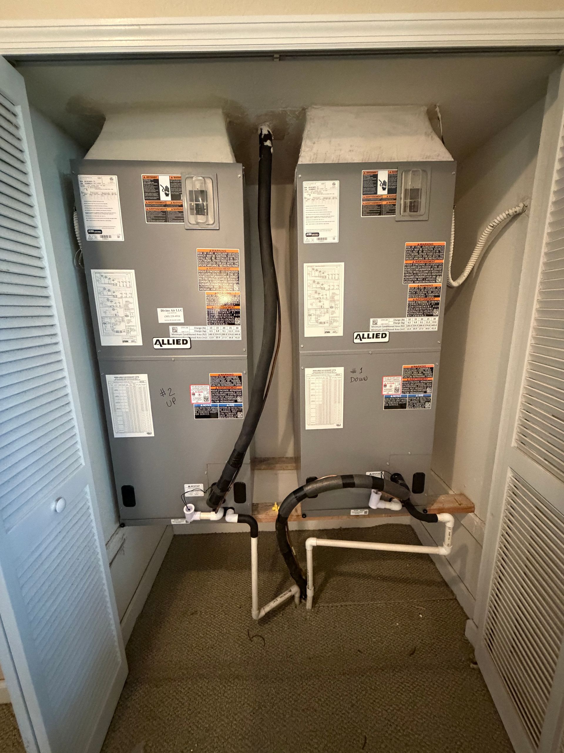 Utility closet with two gray HVAC units and exposed pipes inside a cabinet-like enclosure.