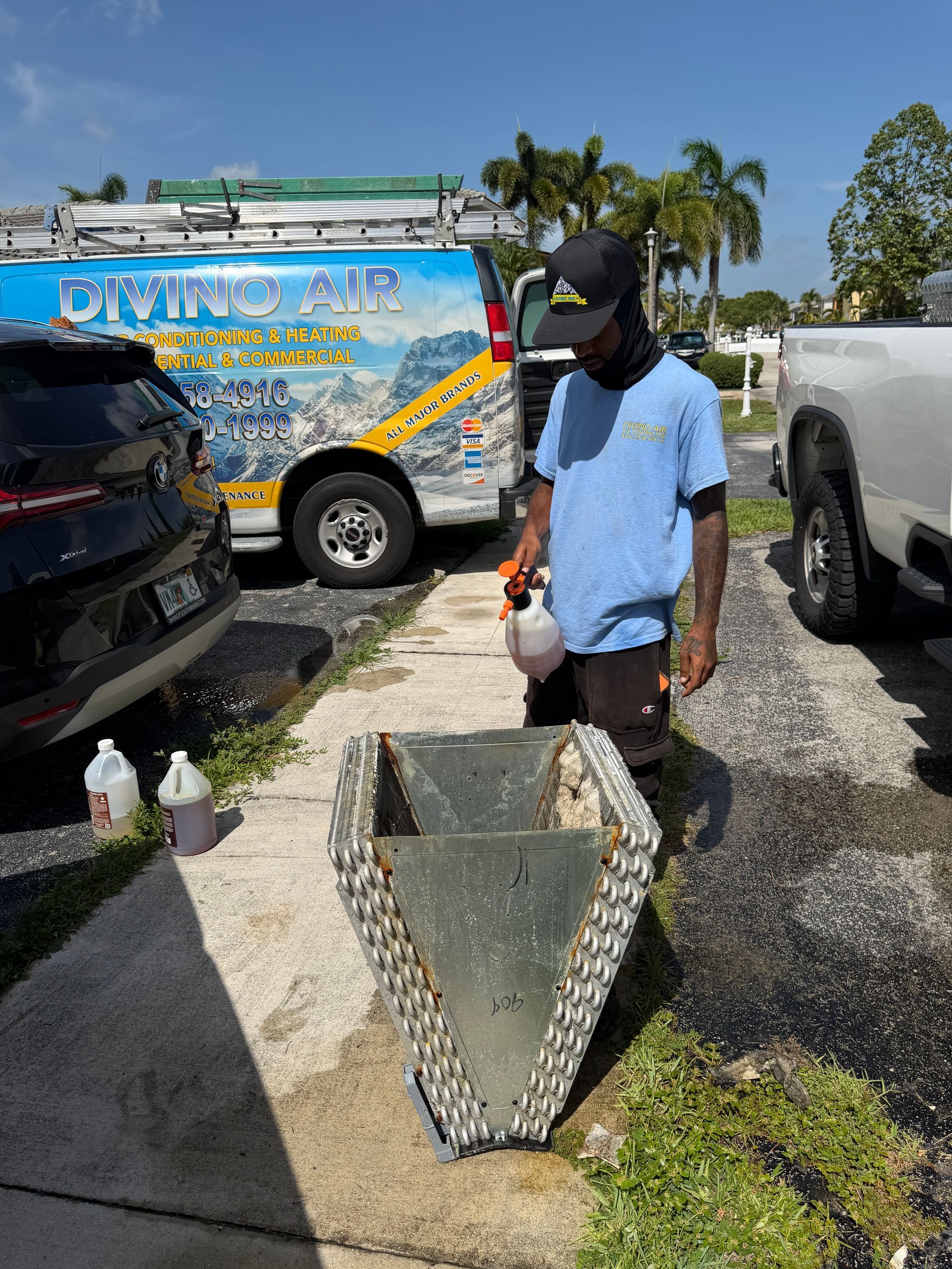 Man standing beside a concrete planter in a driveway, with parked vehicles and a truck in the background