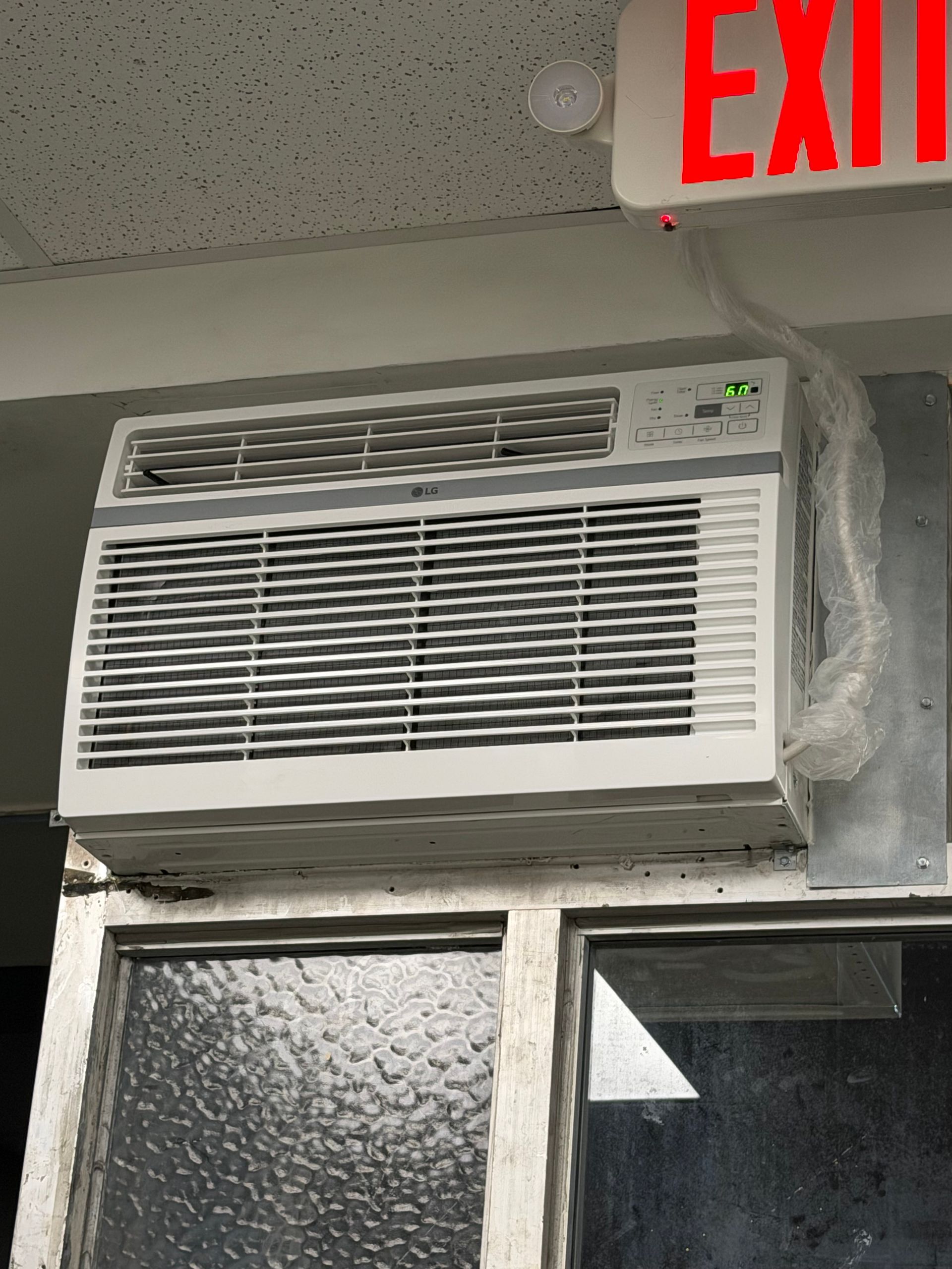 Window air conditioner mounted above a doorway under a red EXIT sign.