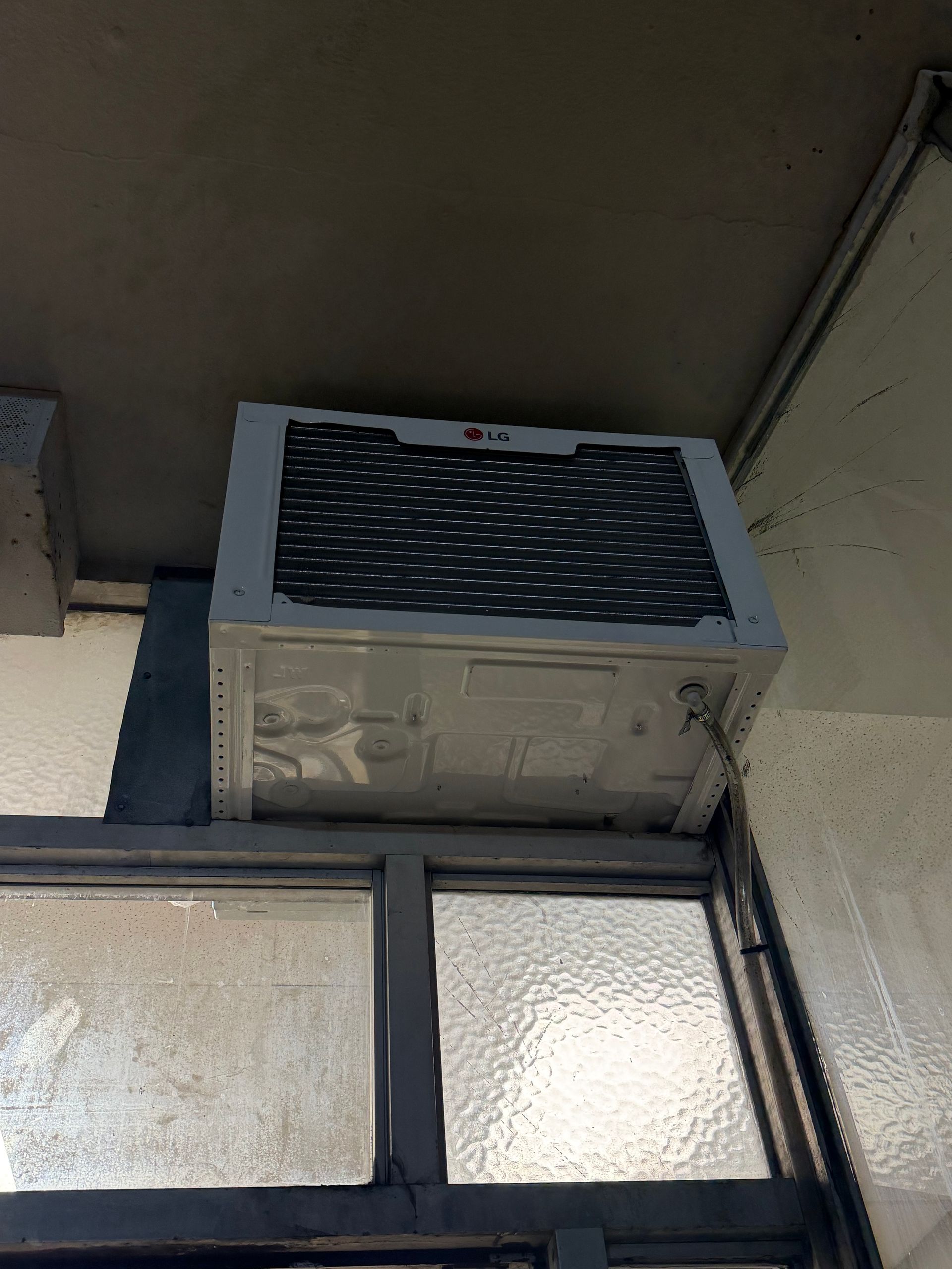 Wall-mounted air conditioner above frosted glass windows under an overhang