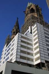 Torre do relógio histórica sob andaimes ao lado de um prédio moderno listrado contra um céu azul.