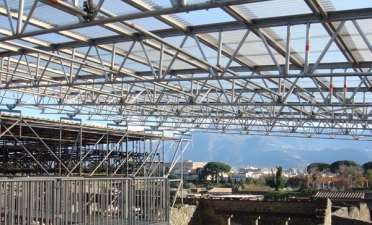 Estufa com estrutura metálica em construção, com andaimes e vista para a montanha ao longe.