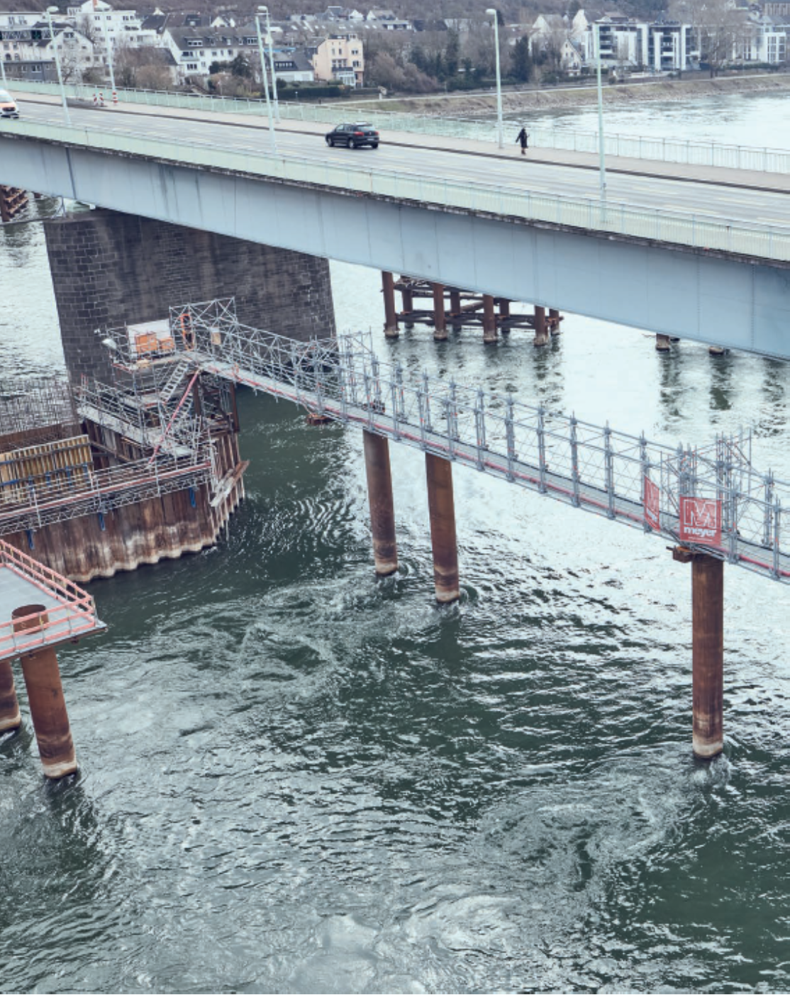 Ponte sobre a água com passarela para pedestres e pequeno barco embaixo, vista de cima.