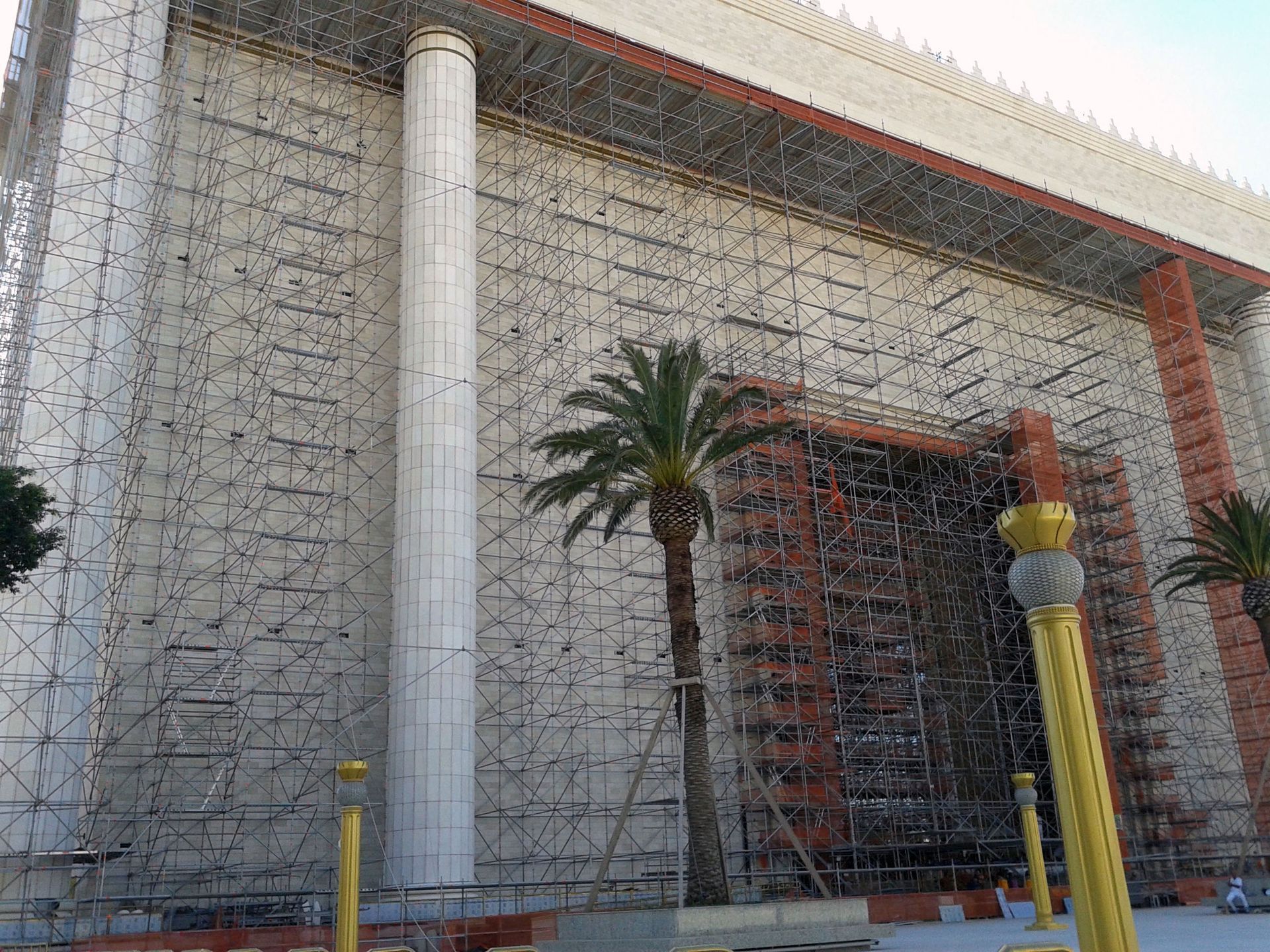 Fachada de edifício moderno com paredes estampadas, uma palmeira e uma entrada com treliça vermelha.