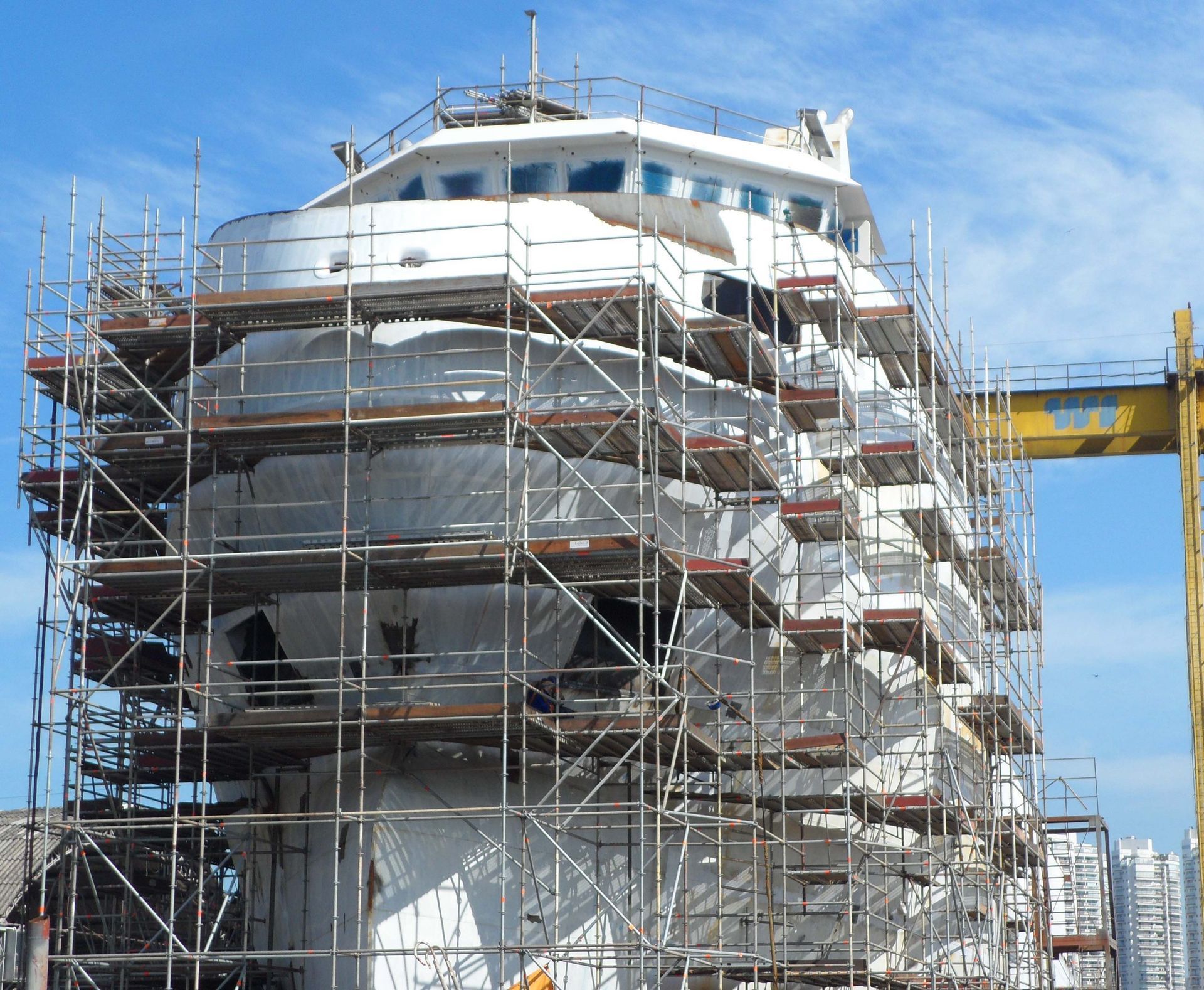 Grande navio branco em construção, cercado por andaimes em um estaleiro.
