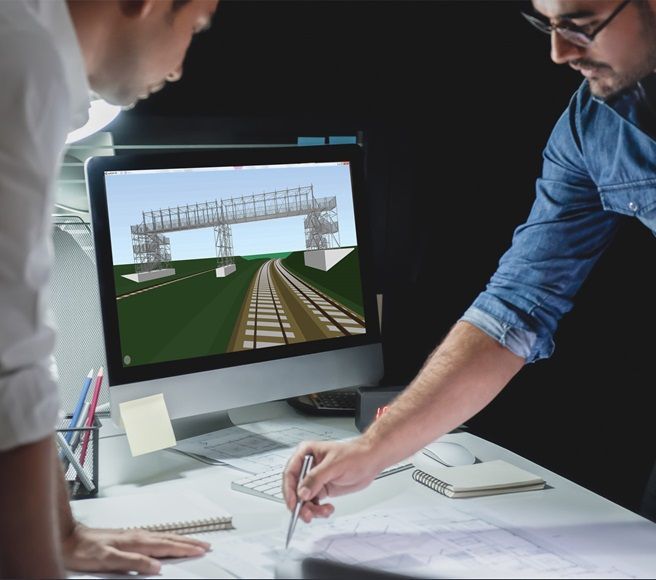 Duas pessoas examinam a tela de um computador que exibe o projeto e os planos de uma linha férrea sobre uma mesa.