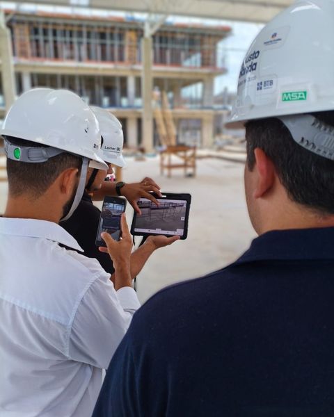 Dois operários com capacetes de segurança analisando um tablet em um canteiro de obras.