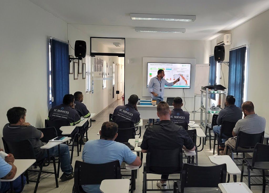 Sessão de treinamento em sala de aula, com um instrutor apresentando o conteúdo para participantes sentados.