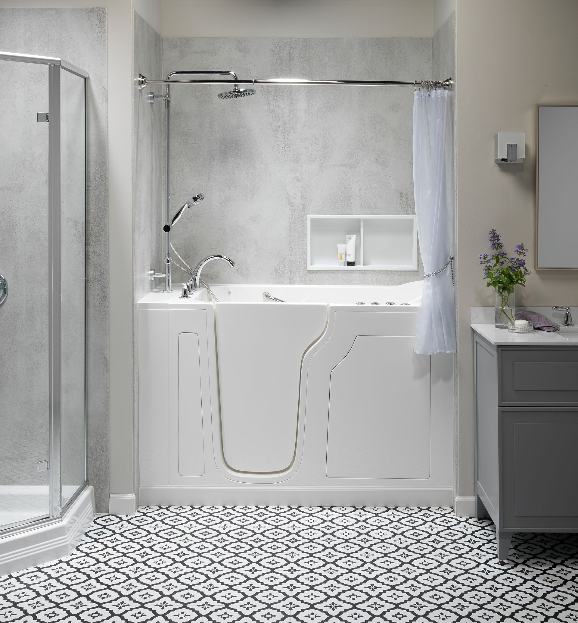 Accessible bathroom with walk-in tub, glass shower, patterned tile floor, and gray vanity