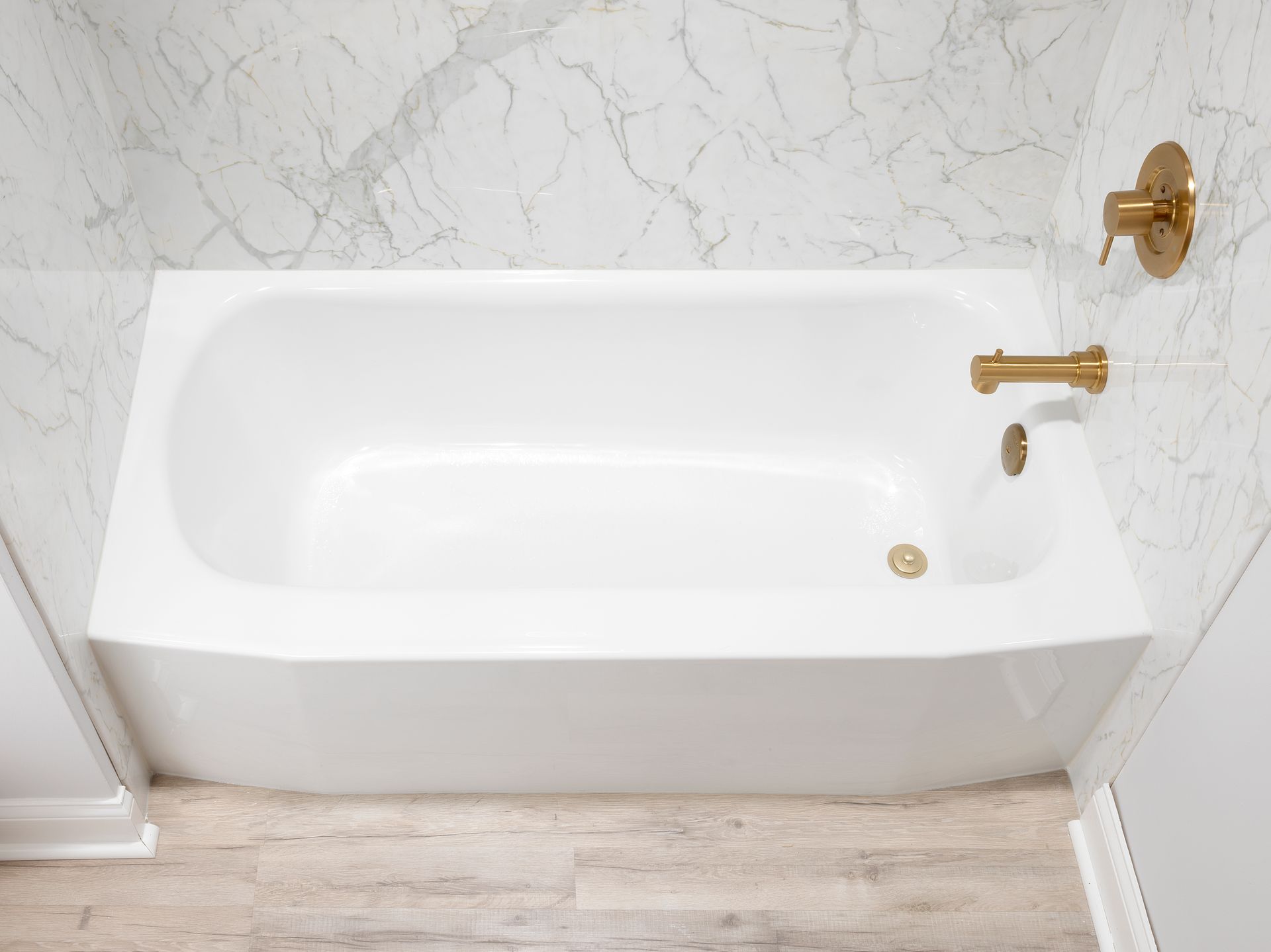 White bathtub with brass fixtures in a marble-tiled bathroom
