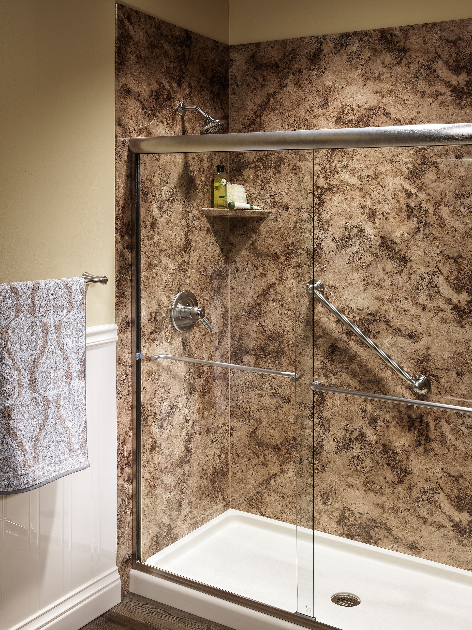 Accessible walk-in shower with beige tile walls, glass panel, grab bar, shelf, and towel on the side.
