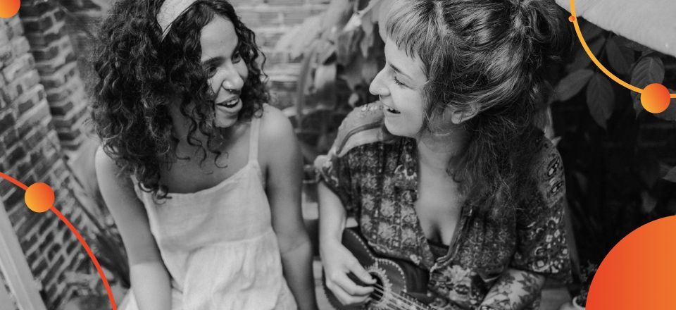 Duas mulheres estão sentadas uma ao lado da outra e rindo em uma foto em preto e branco.
