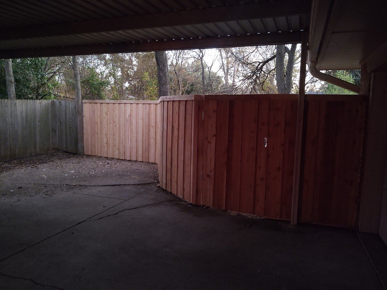 Covered driveway with a wooden fence and concrete ground in dim light