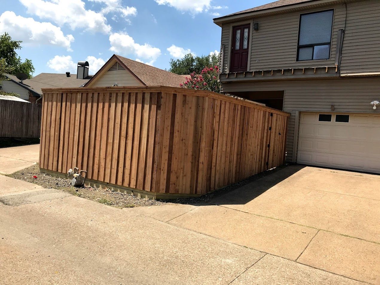 Wooden fenced enclosure beside a house and garage on a concrete driveway under a sunny sky