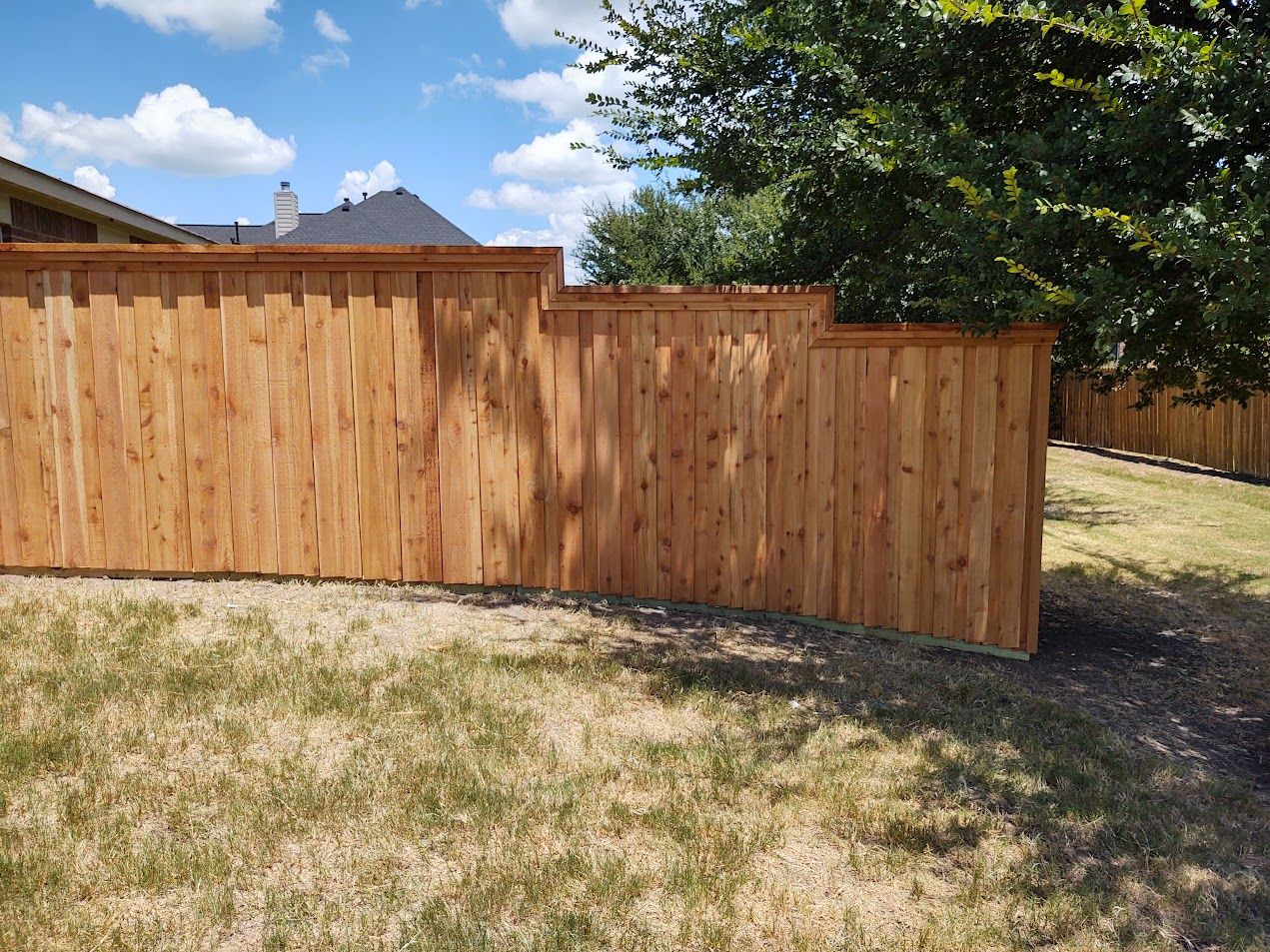 Wooden privacy fence along a grassy yard under a partly cloudy sky.