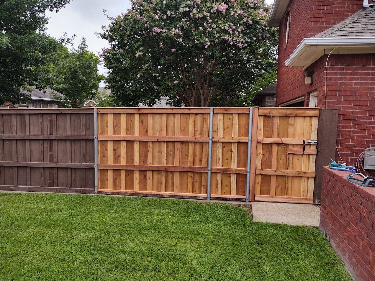 Backyard with wooden fence, green lawn, and red brick house corner