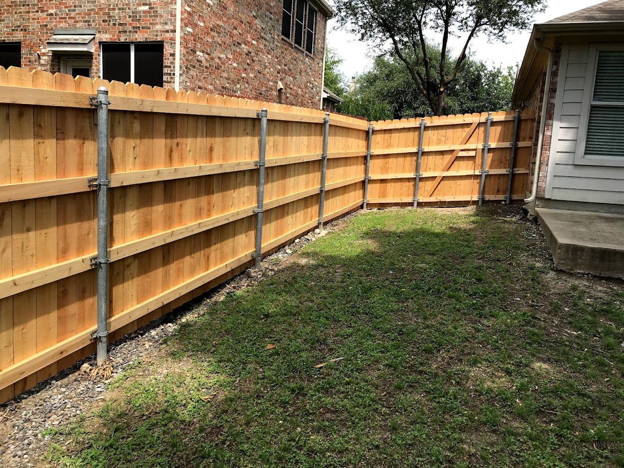 Backyard with wooden privacy fence, grassy lawn, and brick house beside a shed.