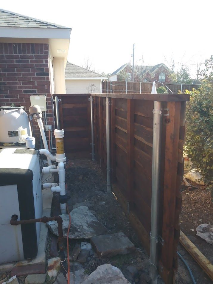 Narrow backyard side yard with utility pipes, a brick house, and a wooden fence alongside a concrete path