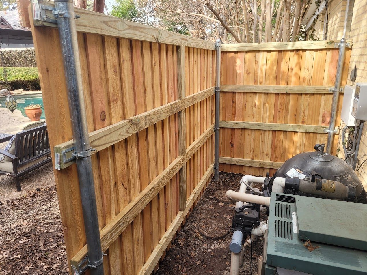 Wooden backyard fence enclosure beside a pool pump and pipes in a narrow gravel area