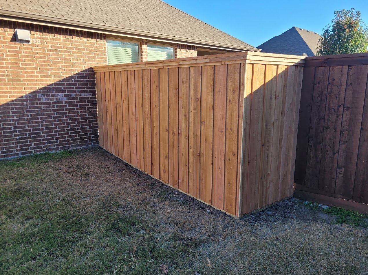 Wooden backyard privacy fence beside a brick house on a grassy lawn.