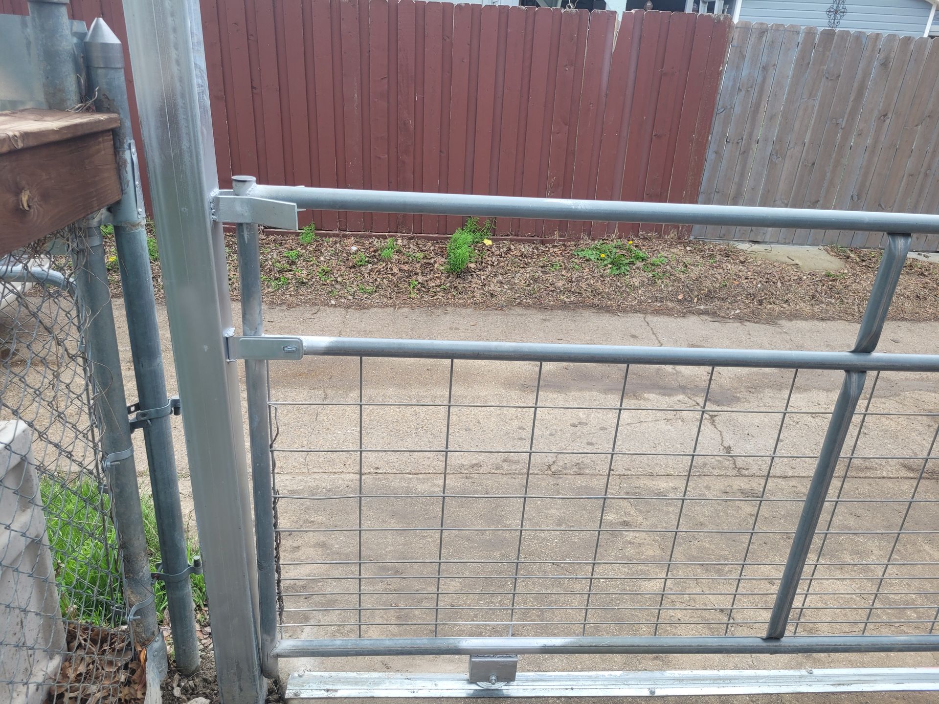 Metal gate and chain-link fence in a yard with a brown wooden fence and gravel beyond.