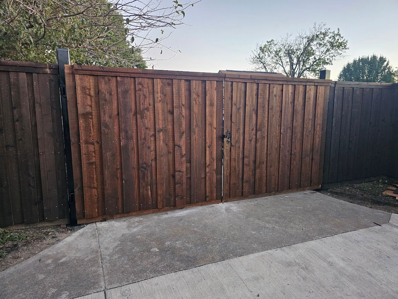 Wooden fence with dark posts beside a paved driveway, under a cloudy sky.
