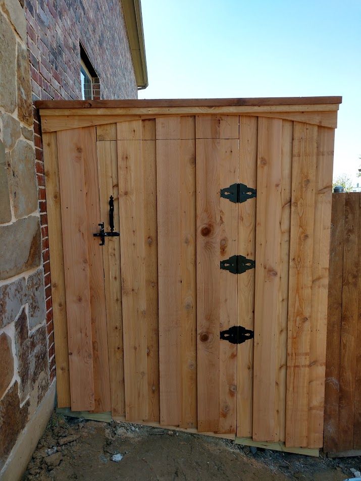 Wooden outdoor gate beside a stone wall, with black iron hinges and latch.