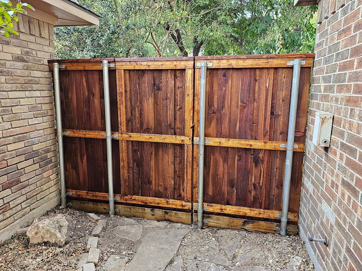 Weathered wooden double gate between brick walls on a gravel driveway.