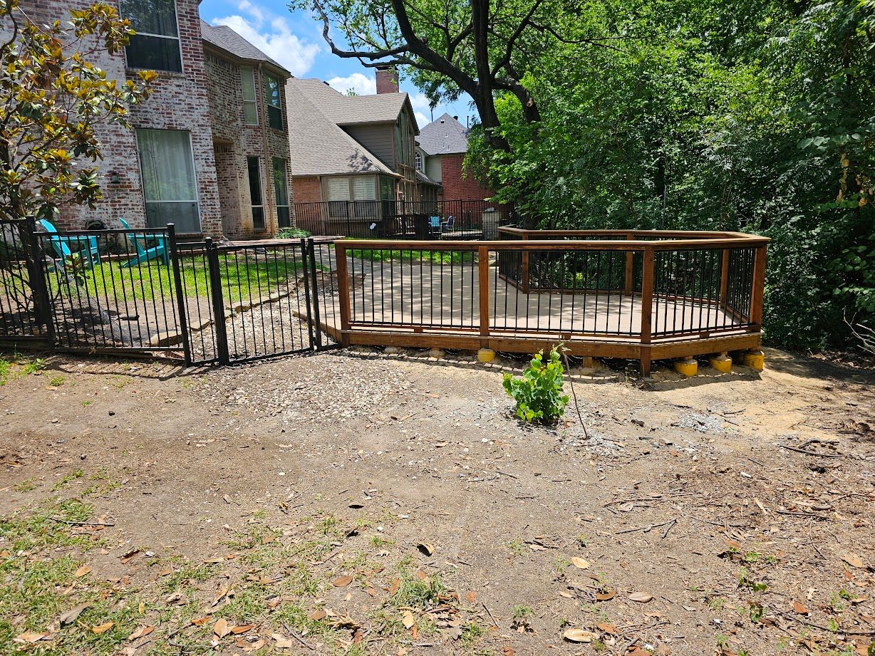 Stone house with a wooden deck and black metal fence in a sunny yard
