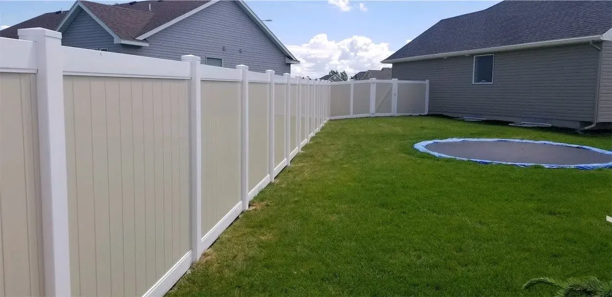 White vinyl fence along a green backyard beside a house, with a round trampoline in the yard.