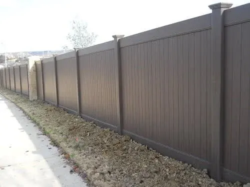 Brown privacy fence along a sidewalk beside a narrow strip of dirt and grass