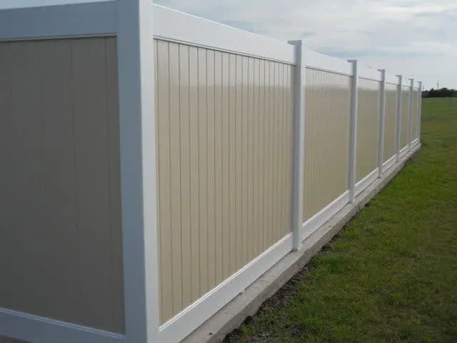 White vinyl privacy fence with beige panels along a grassy field
