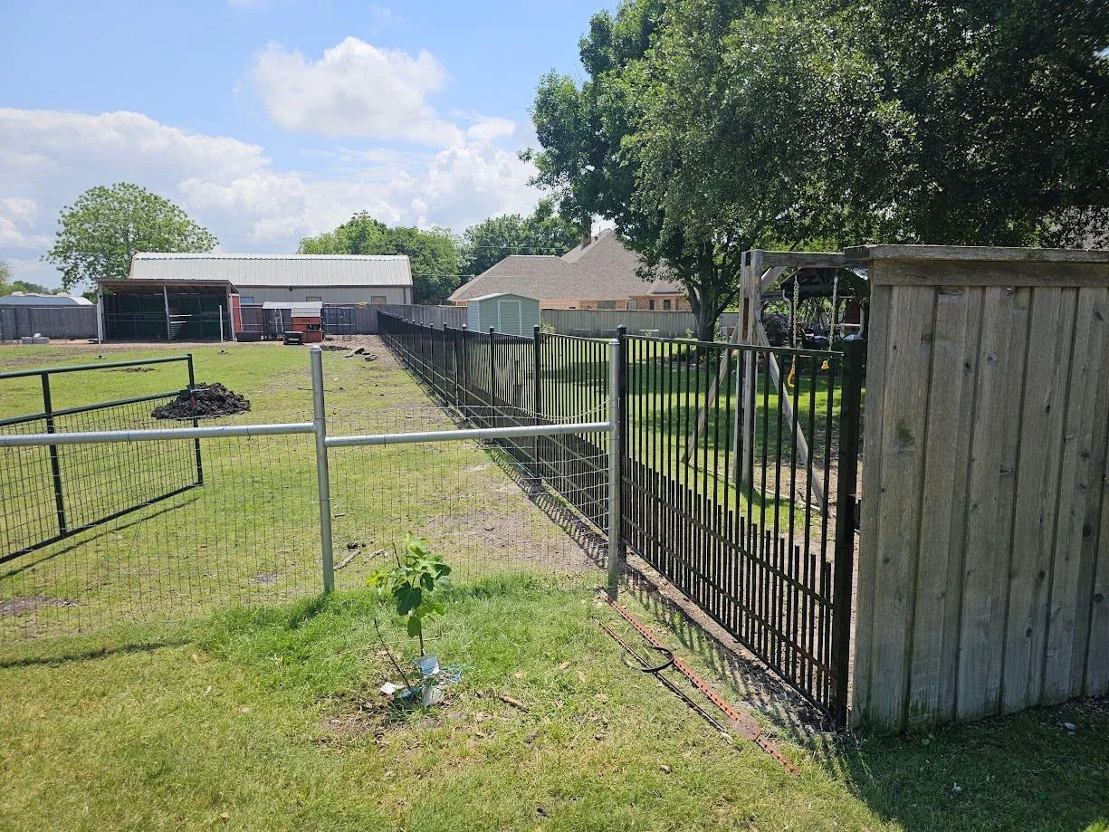 Backyard with a black metal fence, grassy yard, wooden shed, and trees under a partly cloudy sky