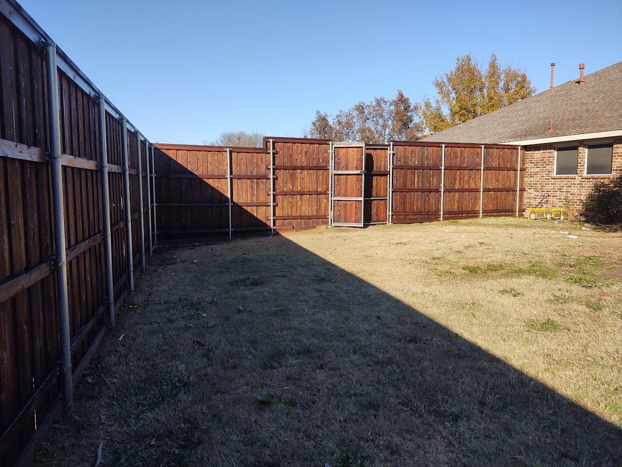 Backyard with wooden fence, grass, and a house in sunlight and shadow