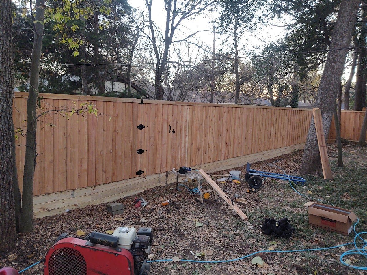 Wooden privacy fence with trees behind it and a cluttered yard in the foreground