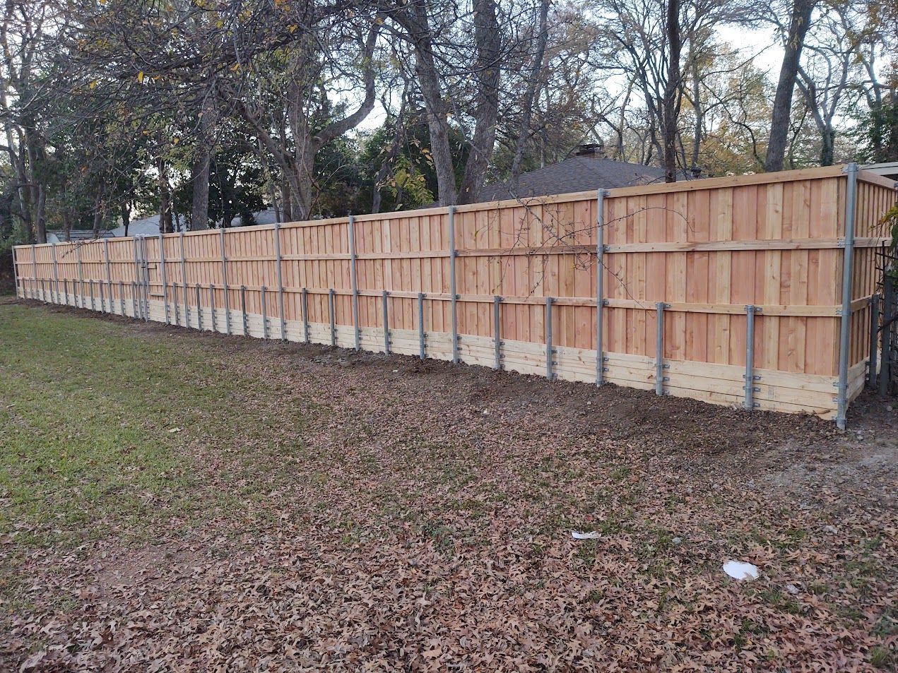 Long wooden privacy fence along a leaf-covered yard with trees in the background