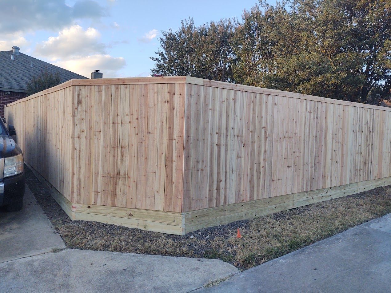 Wooden privacy fence enclosing a yard beside a paved driveway under a clear sky